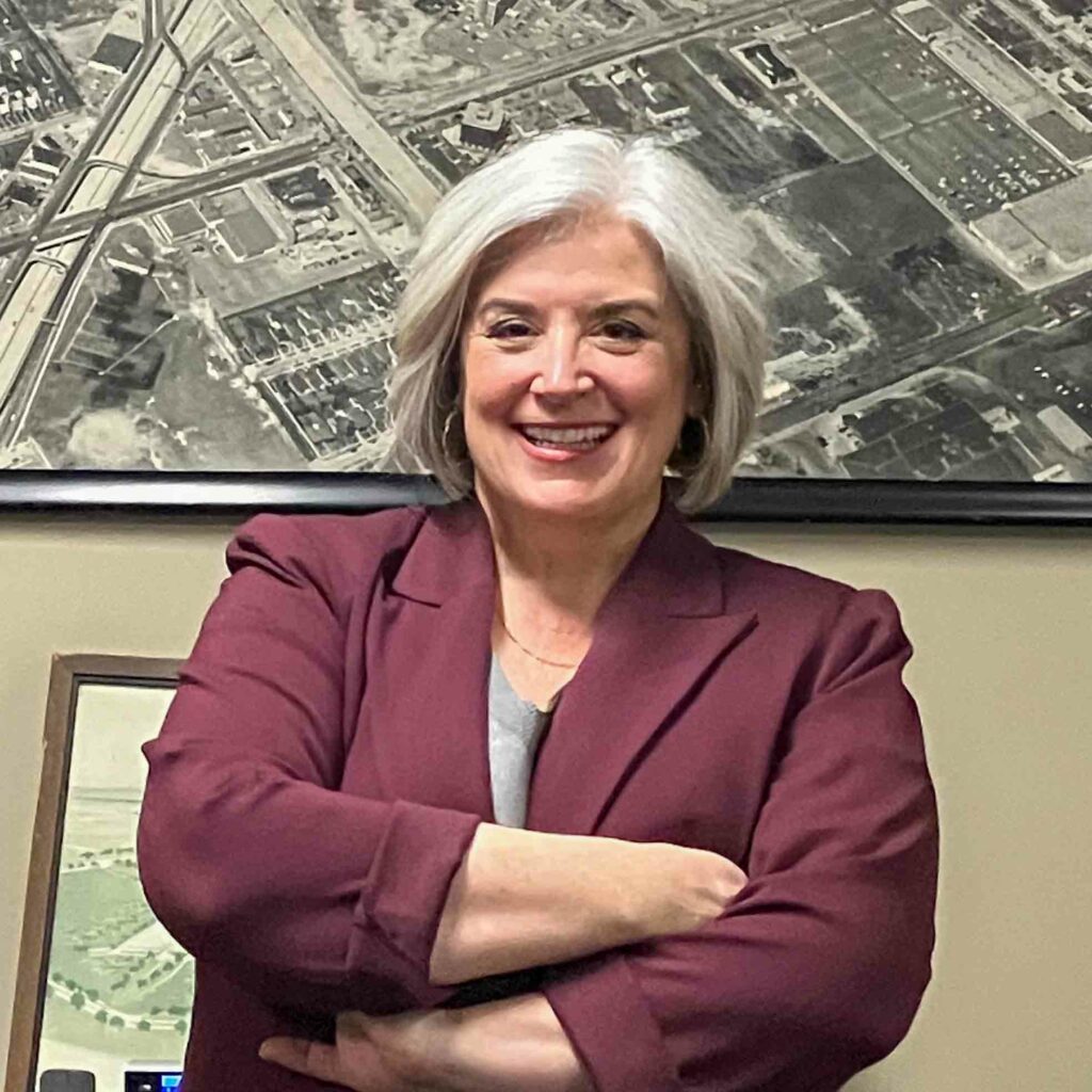 Smiling woman in maroon blazer, arms crossed.