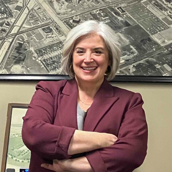 Smiling woman in maroon blazer, arms crossed.
